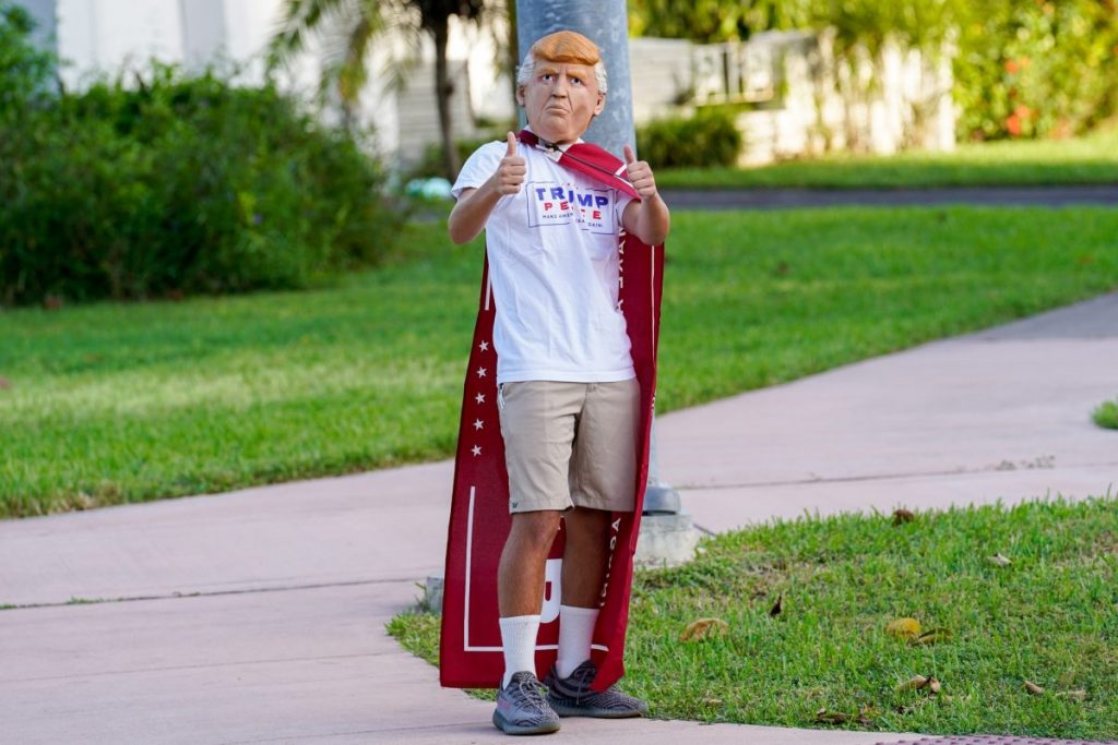 A Trump supporter wearing a Trump mask, shirt, and cape gives a thumbs-up at an intersection near the Coral Gables Library on Tuesday, Nov. 3.