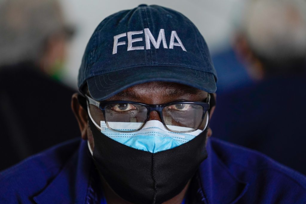 Oladipupo Salau, an emergency management specialist with FEMA, sits at a table in the first registration tent at the FEMA Miami Dade College North Campus vaccination site on March 21, 2021.