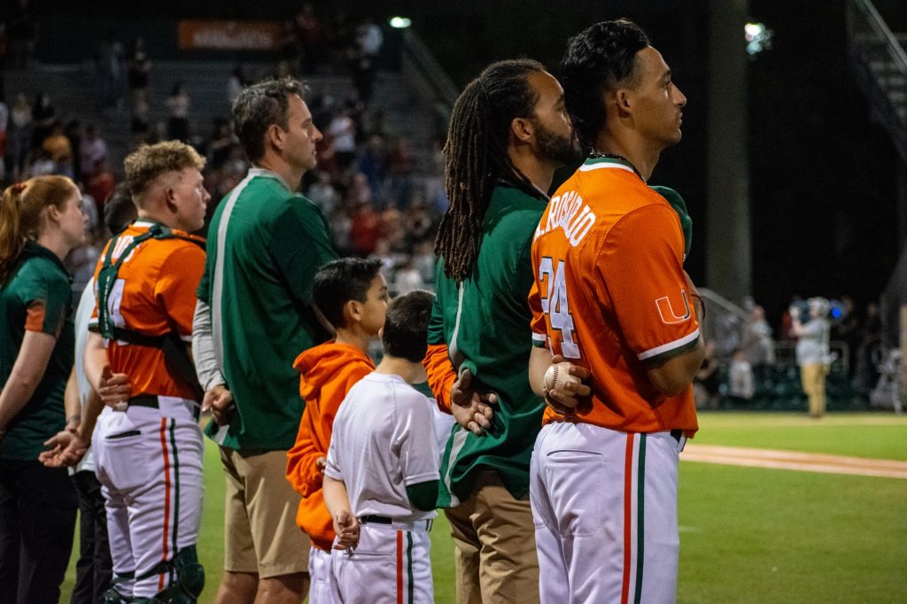 Players and coaches stand for the national anthem before the start of Miami's game versus Harvard at Mark Light Field on Feb. 26, 2022.