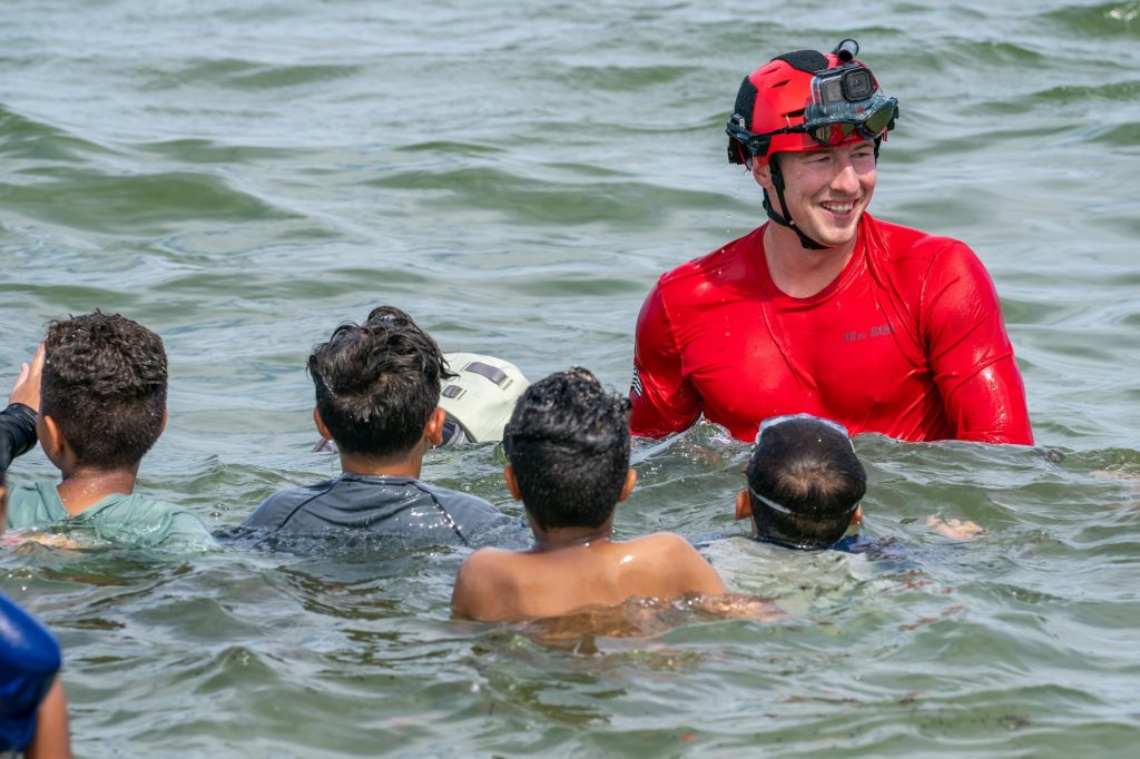 A U.S. Air Force Pararescueman of the 38th Rescue Squadron greets children after swimming to the beach during the 920th Rescue Wing Demonstration at the Hyundai Air and Sea Show at Miami Beach on May 28, 2023.