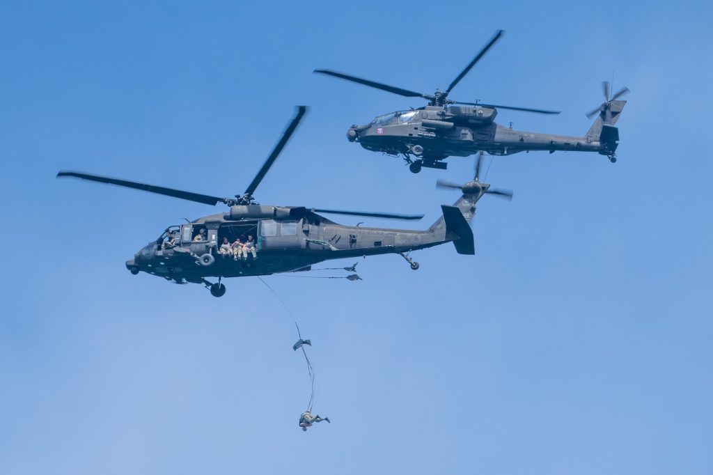 A soldier of the U.S. Army’s Seventh Special Forces Group performs a static-line jump from a UH-60 Black Hawk as an AH-64 Apache circles during the Hyundai Air and Sea Show at Miami Beach on May 28, 2023.