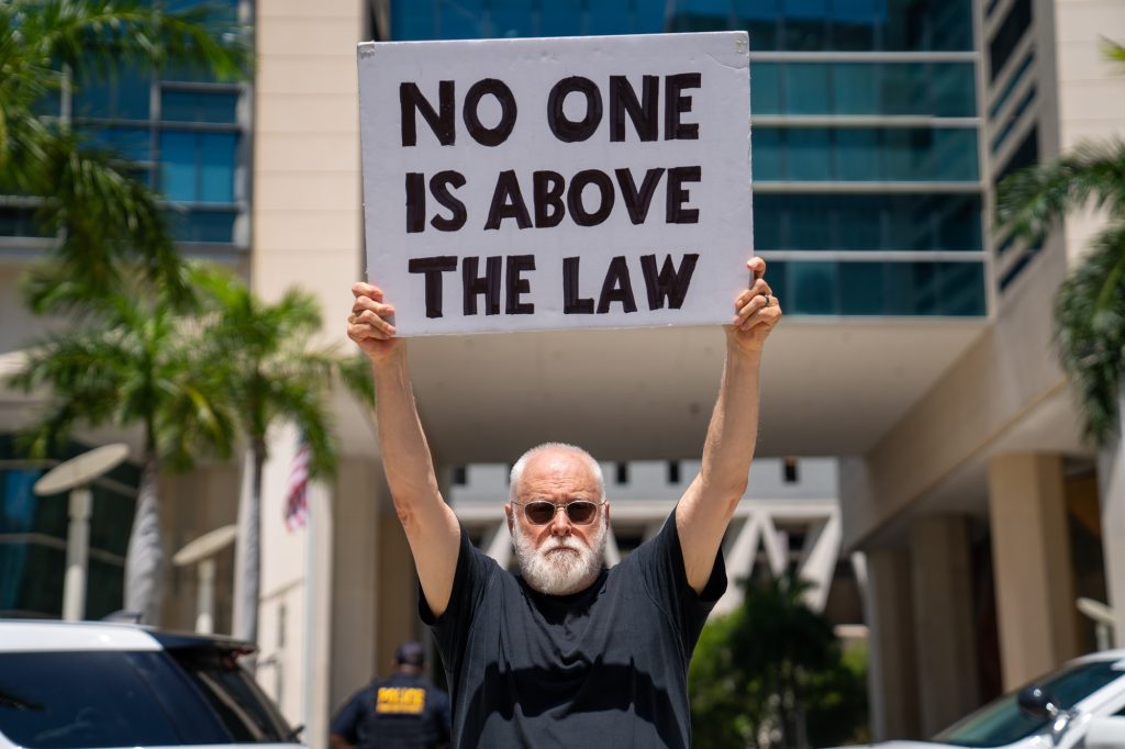 A man holds a sign critical of former President Trump outside of the Wilkie D. Ferguson Jr. United States Courthouse on June 13, 2023.