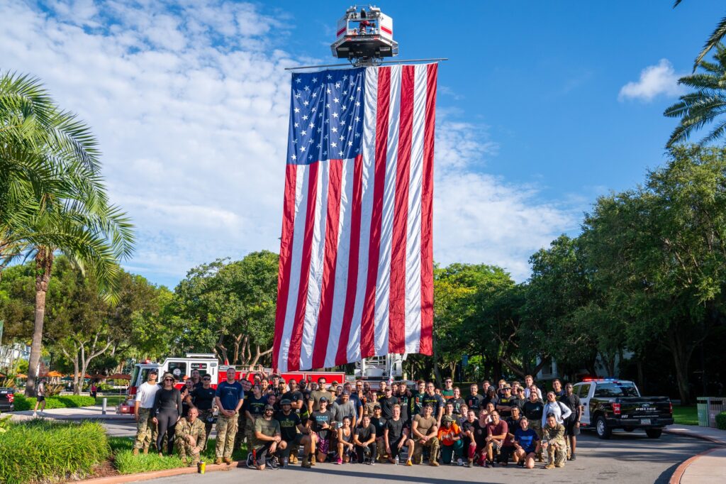 Participants of the 4th annual UM Ruck to Remember pose in front of an American Flag, outside of the undergraduate admissions office, after completing a 9.11 mile-long ruck, to honor the memory of those lost 22-years ago on September 11th.